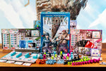 Board game components for Falling including a box, pieces, and cards on a table with a scenic background.